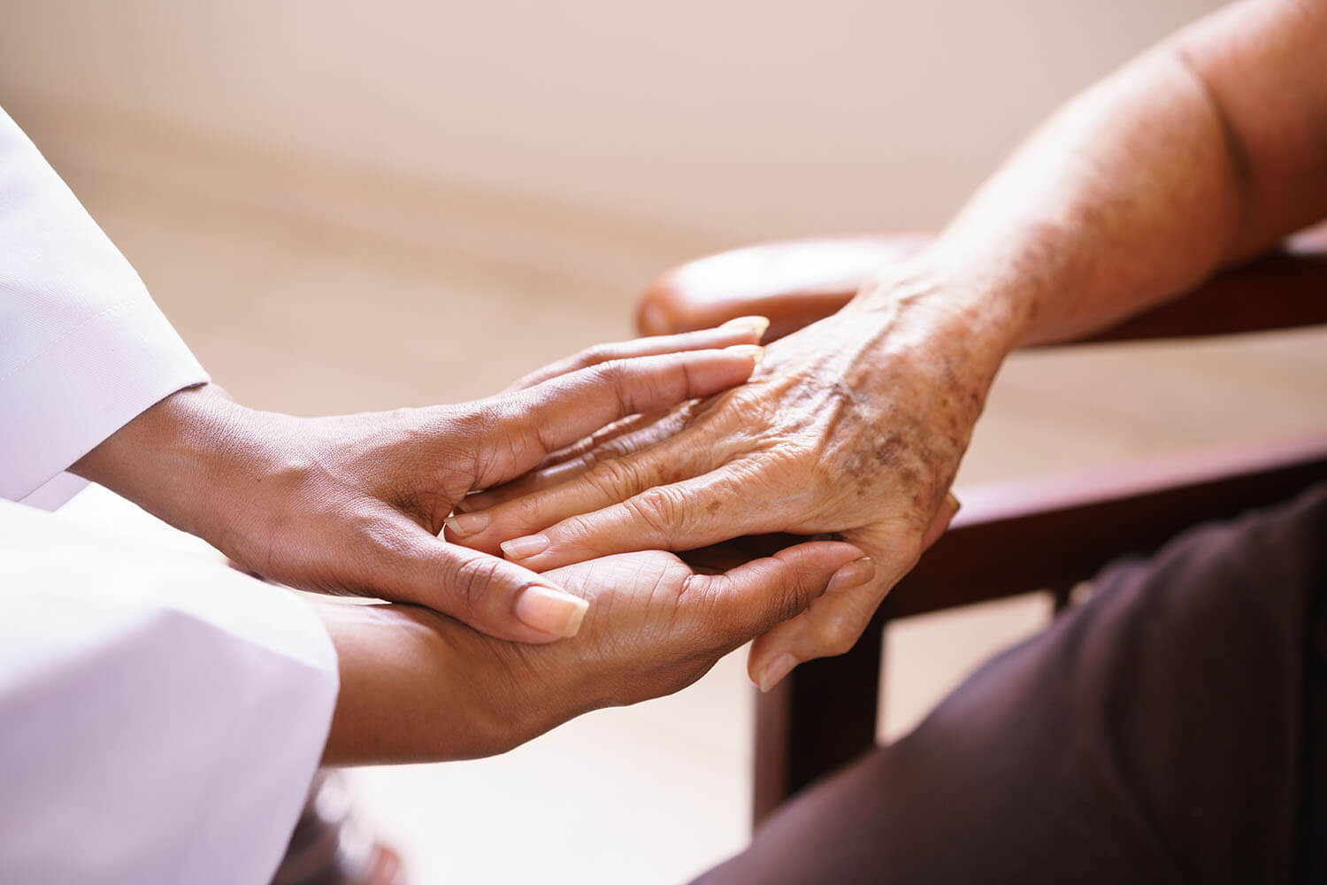 black caregiver holding white senior hand